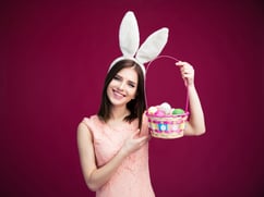 Happy young woman with an Easter egg basket over pink background. Looking at camera
